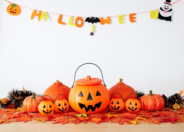 Halloween holiday decoration with pumpkin head jack lantern and autumn leaves on table wood with white wall background, halloween background concept, copy space.