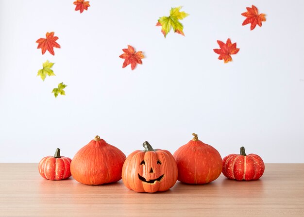 Halloween holiday decoration with pumpkin head jack lantern on table wood with white autumn leaveswall background, halloween background concept, copy space.