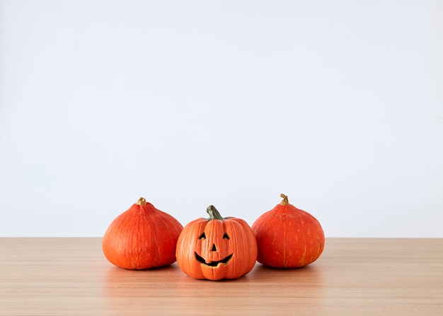 Halloween holiday decoration with pumpkin head jack lantern on table wood with white wall background, halloween background concept, copy space.
