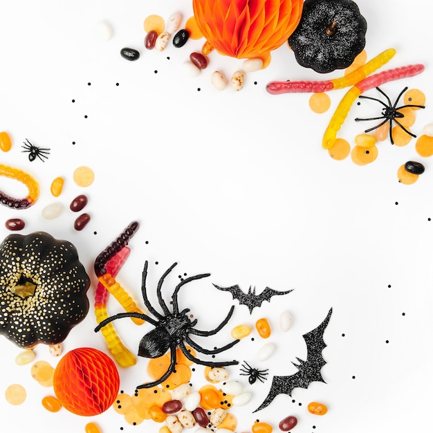 Halloween holiday frame with colorful candy, bats, spiders, pumpkins and decoration on white background. Flat lay. View from above