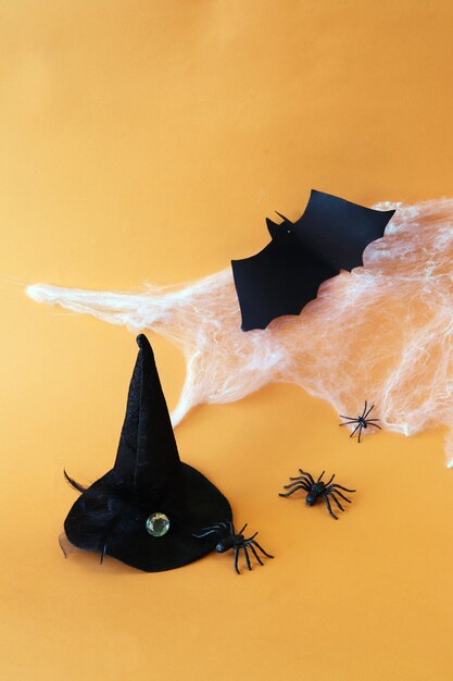 Halloween holiday witch hat cobweb and black spiders on an orange background