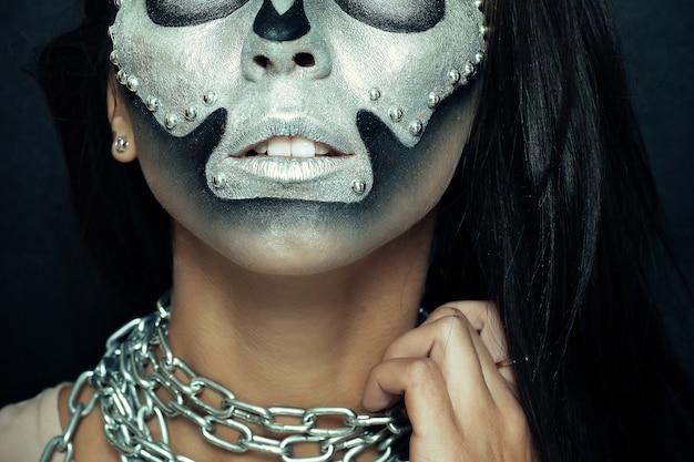Хэллоуин, праздники, образ жизни, люди, красота, креативная концепция. Тема Хэллоуина и креативного макияжа: красивая девушка с черным телом и серебряной маской с черепом на темном фоне в студии.