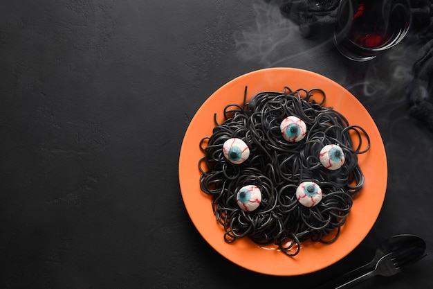 La pasta nera italiana di halloween ha decorato gli occhi di orrore in piatto arancio sul nero