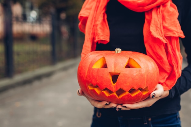 Halloween jack-o-lantern pumpkin. Woman holds hand-made carved pumpkin outdoors. Close up