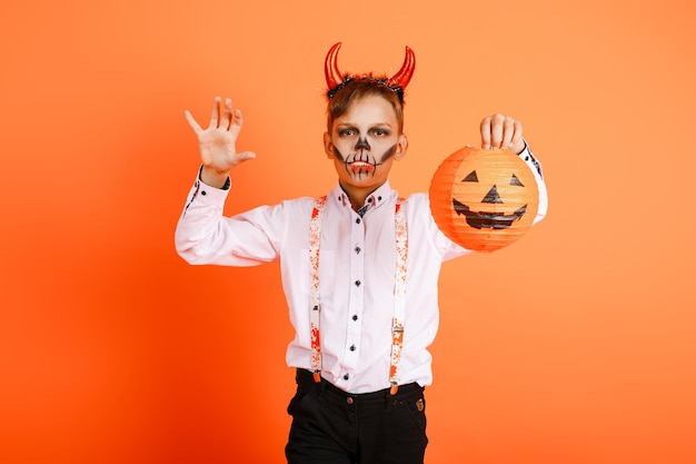 Halloween-jongen met duivelshoorns maakt een eng gebaar op de achtergrond van een oranje muur. Hoge kwaliteit foto