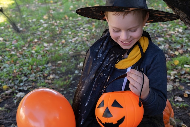 Дети Хэллоуина. Милый маленький мальчик, ребенок в шляпе ведьмы с оранжевым ведром конфет Jack O Lantern. Счастливого Хэллоуина.