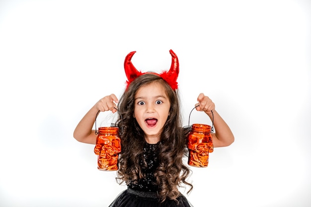 Halloween kidsCurly little girl in a witch costume with skull lanterns on a white studio backgroun