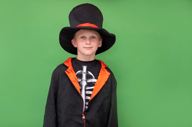 Halloween-kinderen Een jongen in een skeletkostuum houdt een jack o lantern Groene achtergrond Kopieer ruimte Een kind in een zwarte jas hoed houdt een halloween-pompoen vast Plaats voor tekst