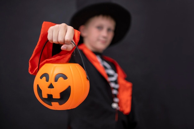 Halloween-kinderen Een jongen in een skeletkostuum houdt een jack o lantern Zwarte achtergrond Kopieerruimte Een kind in een zwarte jas hoed houdt een halloween-pompoen vast Plaats voor tekst