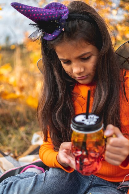 Halloween-kinderen. Portret verveeld meisje met bruin haar in heksenhoed met glas.