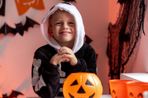 Foto halloween-kinderjongen met pompoensnoepemmers in skeletkostuum thuis klaar voor trick or treat-vakantie