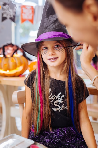 할로윈 메이크업. 할로윈 메이크업을 받고 행복 느낌 마법사 모자를 쓰고 검은 머리 아름다운 귀여운 소녀