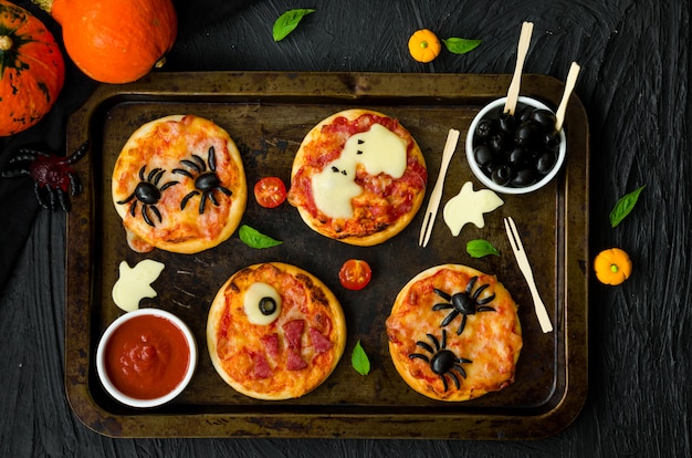 Halloween mini pizza monsters su uno sfondo nero. pizza ragno, pizza fantasma, pizza mostro. idea gastronomica per la festa di halloween.