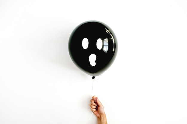 Минимальная концепция Хэллоуина. Один черный шар с страшным лицом в руке девушки