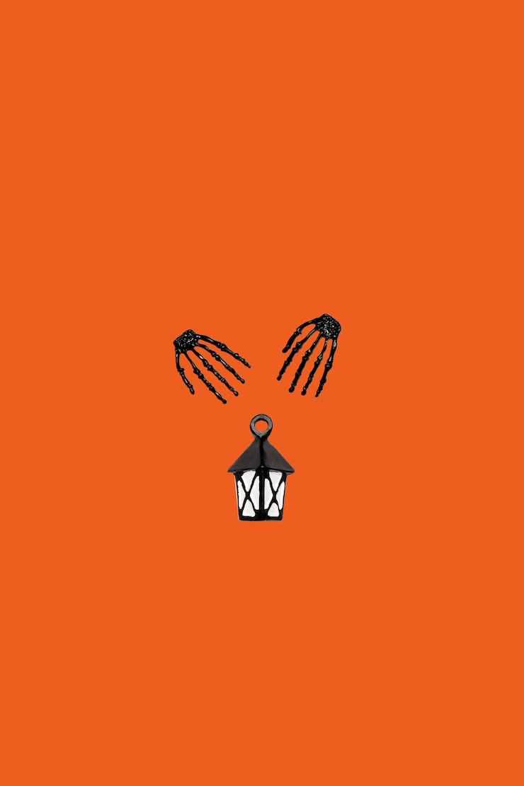 Photo halloween minimal concept with orange background and black skeleton hand holding lantern on wallpaper with copy space holiday autumn idea for party invitation spooky holiday symbol