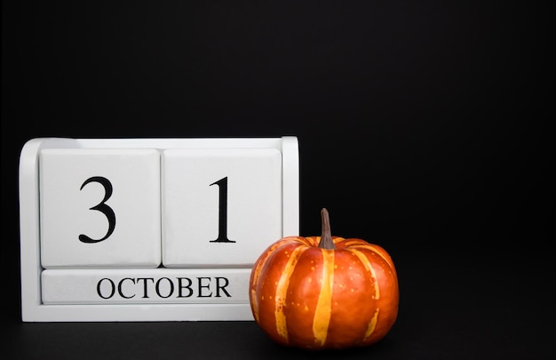 Halloween. October 31 is a white, wooden calendar on an black background, next to it is a pumpkin.