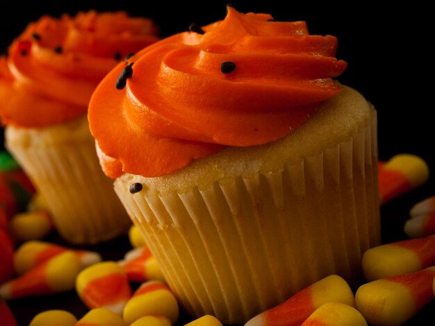 Halloween orange and black cupcakes with candy corn candies on black background.