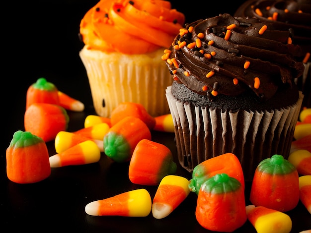 Halloween orange and black cupcakes with candy corn candies on black background.