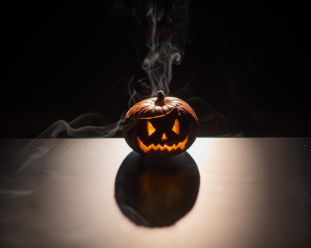 Halloween oranje pompoen met een eng lichtgevend gezicht op een donkere achtergrond Dikke grijze rook komt naar buiten en verspreidt zich over de zwarte tafel Een close-up van een zaklamp aan de vooravond van alle heiligen