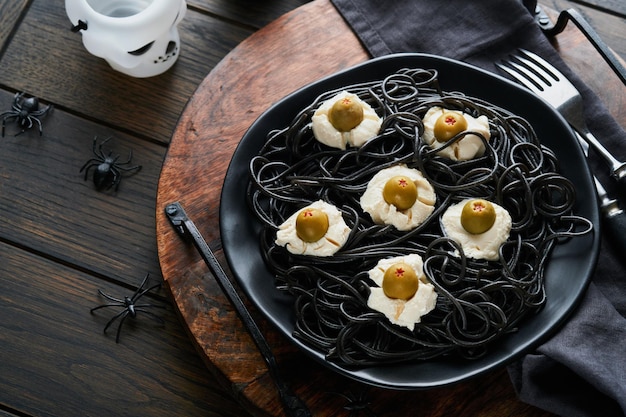 Halloween party Italian black pasta decorated horror olives like eyes on black plate on old dark table background Monster face from pasta Halloween decorations and Halloween food concept Mock up