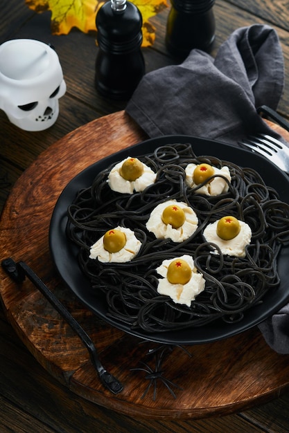 Photo halloween party italian black pasta decorated horror olives like eyes on black plate on old dark table background monster face from pasta halloween decorations and halloween food concept mock up