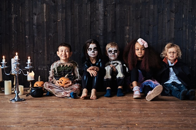 古い家で木製の床に一緒に座っているグループの子供たちとのハロウィンパーティー ハロウィンコンセプト