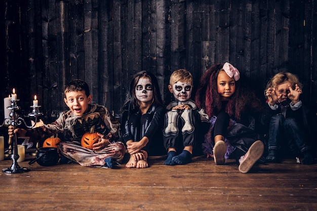 Halloween party with group children who sitting together on a wooden floor in an old house.