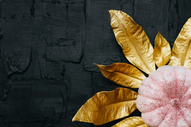 Zucca di halloween glitter rosa e foglie d'oro su sfondo nero