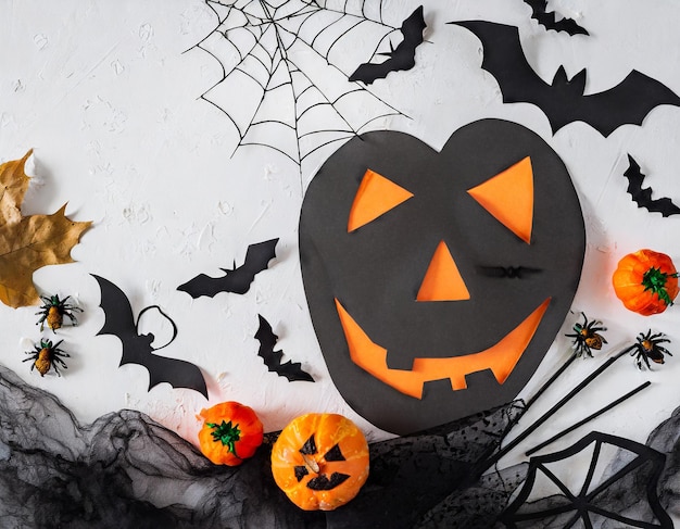 Halloween plat gelegd met pompoenmasker, heksenhoed, vliegende vleermuizen, decoratief web en griezelige geest op