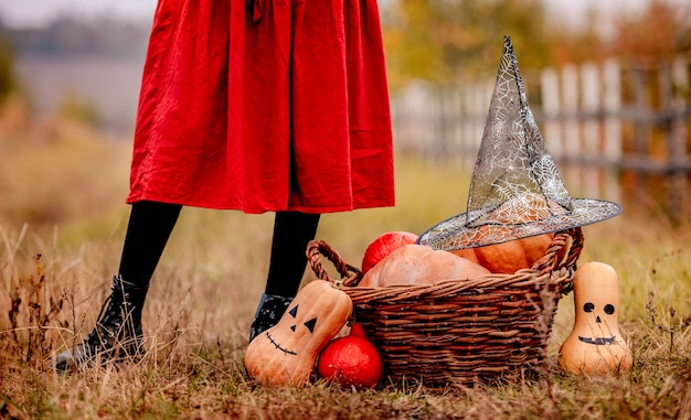 Halloween-pompoenen en mand met heksenhoed die zich bij meisjesvoeten op de herfstgrond bevinden