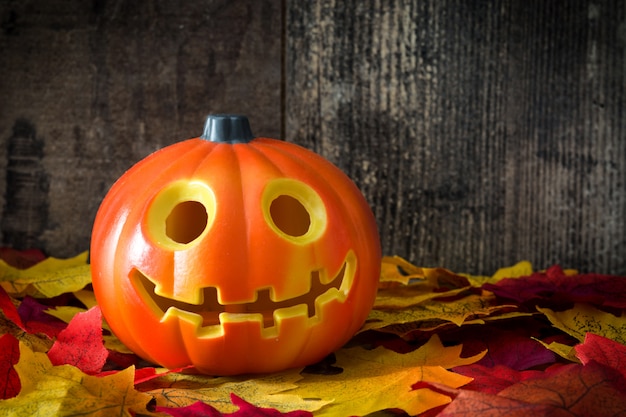 Halloween pumpkin and autumn leaves on wooden background