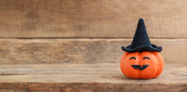 Halloween pumpkin in black hat with funny face on wooden background