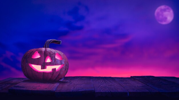 Zucca di halloween jack o lantern su assi di legno contro il cielo rosa e blu con la luna