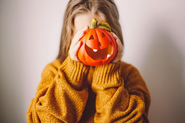 女の子の手にあるハロウィーンのカボチャランプが彼女の顔を覆っている