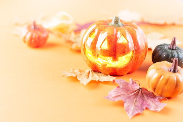 Halloween pumpkin lantern and autumn dry leaves on orange background Halloween and autumn background