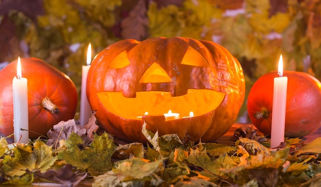 Halloween pumpkin lantern with dry leaves, candles and smoke.