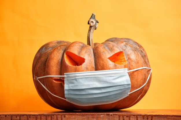 Halloween pumpkin in a medical mask on an orange background