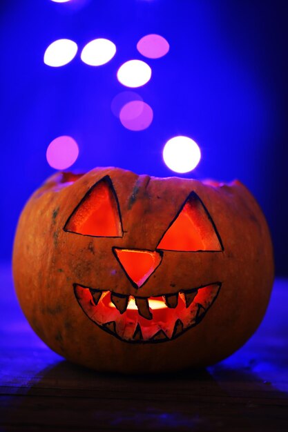Halloween pumpkin on table on dark color background with multicolor lights