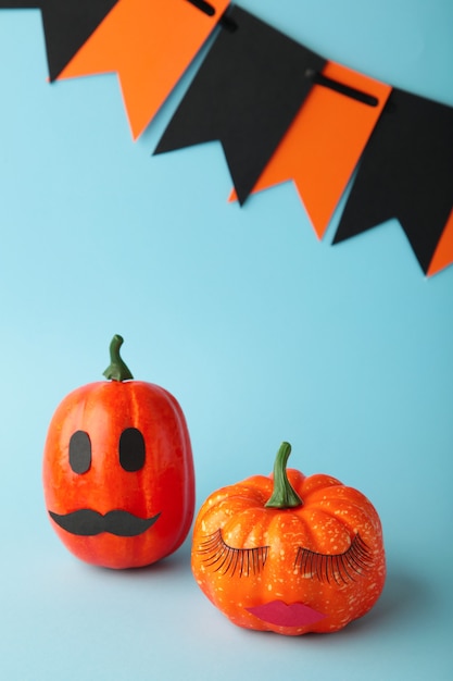 Halloween pumpkin with make up on blue. Minimal Holiday season concept background. Man and woman. Vertical photo