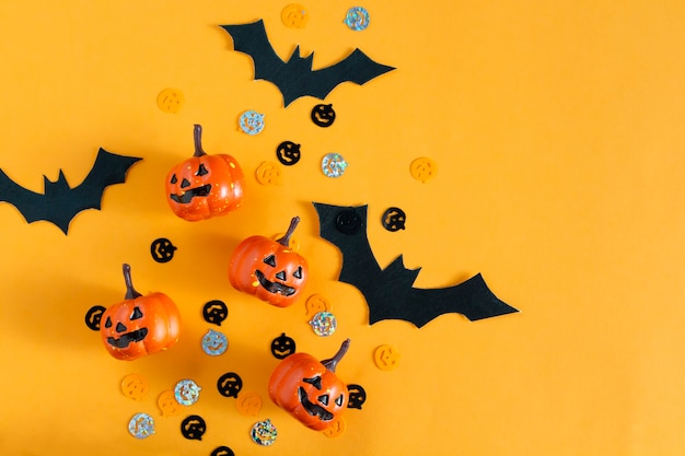 Halloween pumpkins, bats, party objects flat lay on orange background. Top view, copy space.