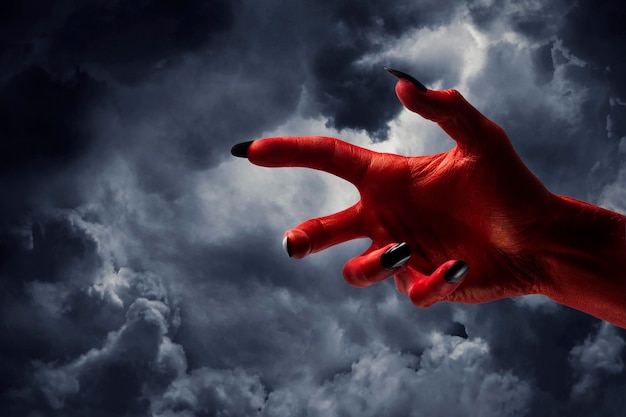 Рука монстра красного дьявола хеллоуина с черными ногтями против темного неба