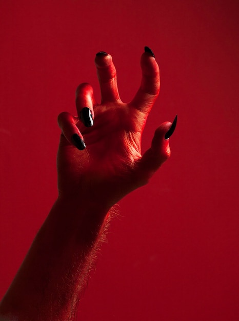 Halloween red devil monster hand with black fingernails against a red background