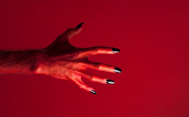 Halloween red devil monster hand with black fingernails against a red background