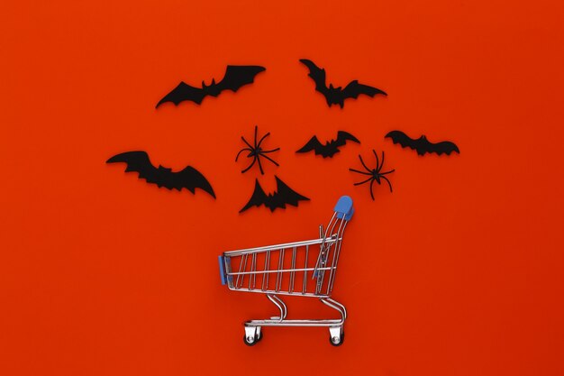 Halloween sale, shopping. Supermarket trolley and flying bats, spiders on orange. Halloween decoration