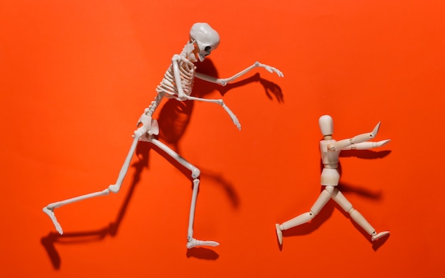 Photo halloween scary concept. wooden puppet runs away from the skeleton on orange bright