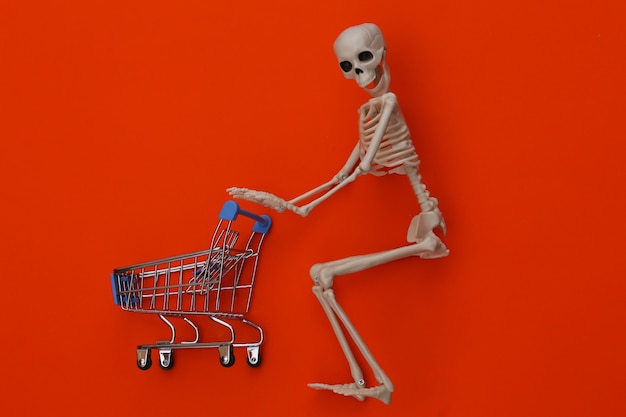 Halloween, scary theme. Skeleton and shopping trolley on orange.