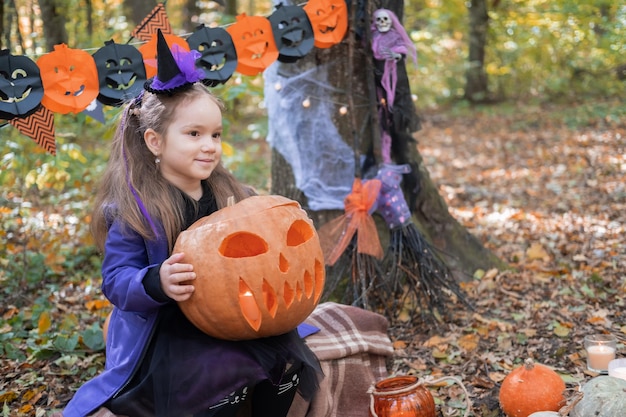 Halloween. schattig klein meisje in heksenkostuum met pompoen die plezier heeft buiten