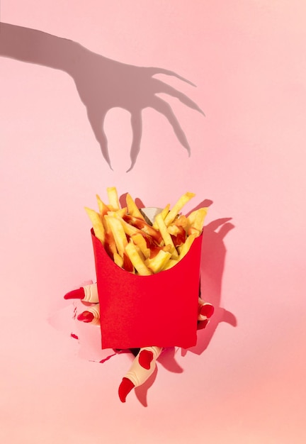 Halloween spooky idea Witch's hand shadow and french fries in paper box against pink background