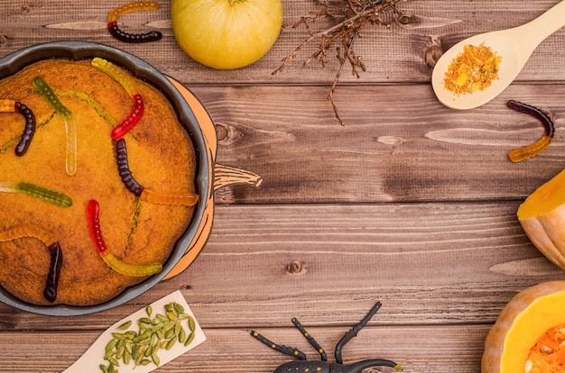 Halloween surface with copy space: pumpkin pie with orange pumpkins,  with sweet worms, spider, on a wooden surface