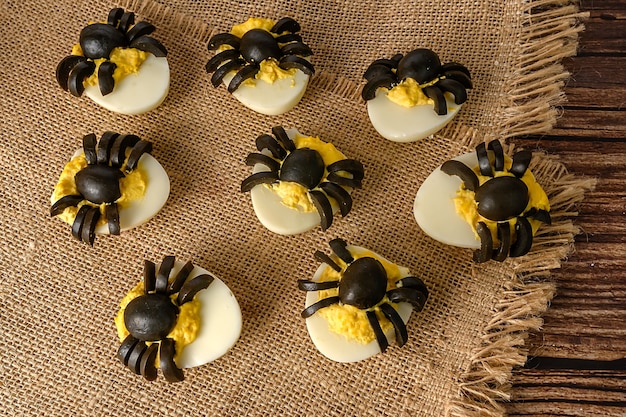 Halloween table decoration. Spiders made from eggs and olives. Party snack. On sackcloth.